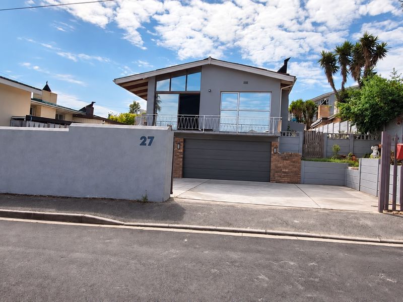 Front view of a modern house featuring a double garage, a balcony with metal railings, and a clean concrete driveway.