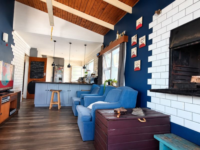 Open-plan living area featuring a built-in fireplace with subway tile surround, exposed timber beam ceiling, and a functional kitchen island with pendant lighting.