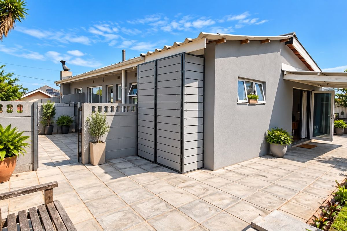 A well-maintained rear exterior view featuring a paved patio area, concrete boundary walls, and a modern external storage unit.
