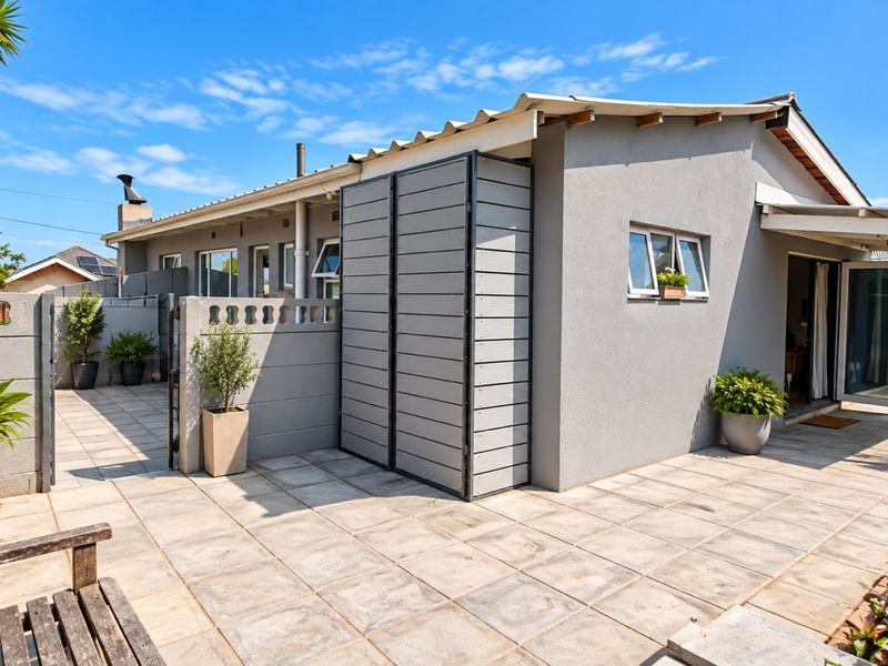 A well-maintained rear exterior view featuring a paved patio area, concrete boundary walls, and a modern external storage unit.