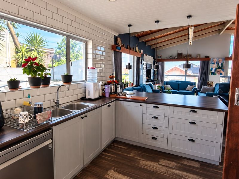 Open plan kitchen and living area featuring shaker style cabinetry, subway tile backsplash, dark laminate countertops, and exposed timber ceiling beams.
