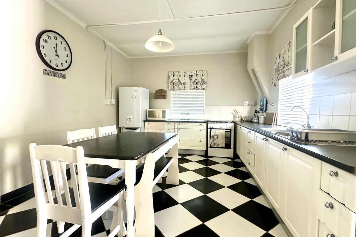 A functional kitchen featuring classic checkerboard flooring, white cabinetry, a tiled backsplash, and a built-in cooker, offering a clean and traditional aesthetic.