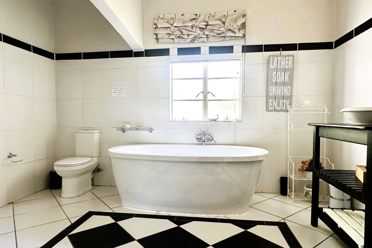 A well-maintained bathroom featuring a classic black and white tiled floor, a central freestanding bathtub, and neutral wall tiling.