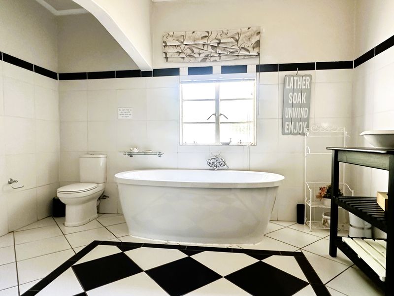 A well-maintained bathroom featuring a classic black and white tiled floor, a central freestanding bathtub, and neutral wall tiling.