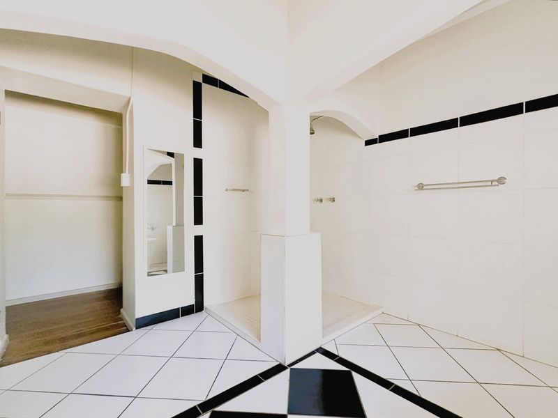 A spacious, empty bathroom featuring a walk-in shower with white and black tiled finishes, providing a clean and functional layout.