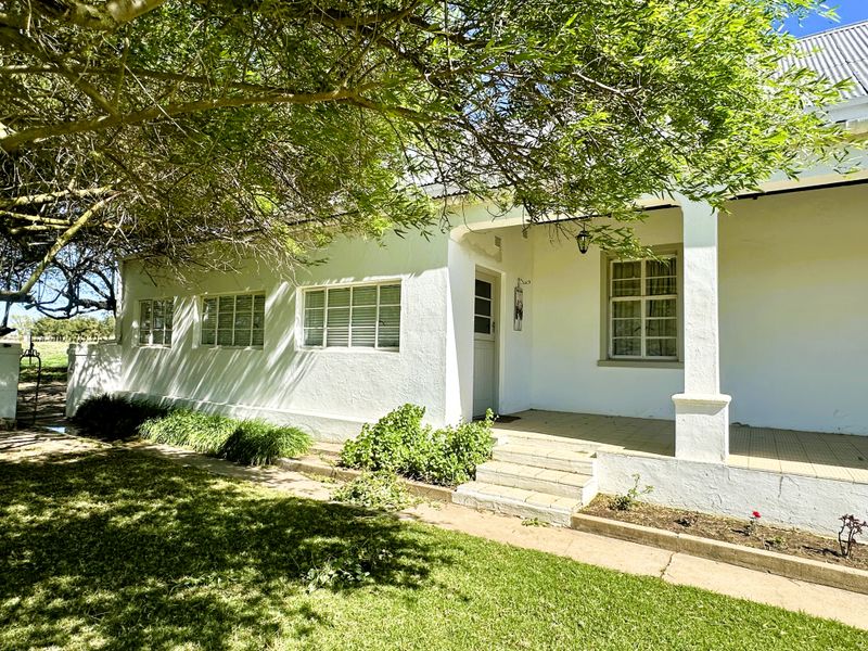 A charming front facade of a townhouse featuring a covered veranda, tiled patio, and classic casement windows set within a landscaped garden.
