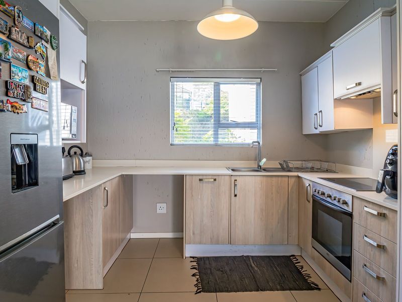 A functional kitchen featuring light wood-finish cabinetry, laminate countertops, a built-in oven with hob, and tiled flooring, offering a practical layout for daily use.