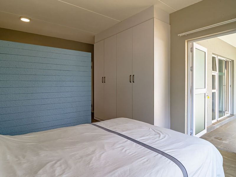 A well-maintained bedroom featuring built-in cupboards, neutral wall tones, and direct access to an outdoor balcony area through a glass panel door.