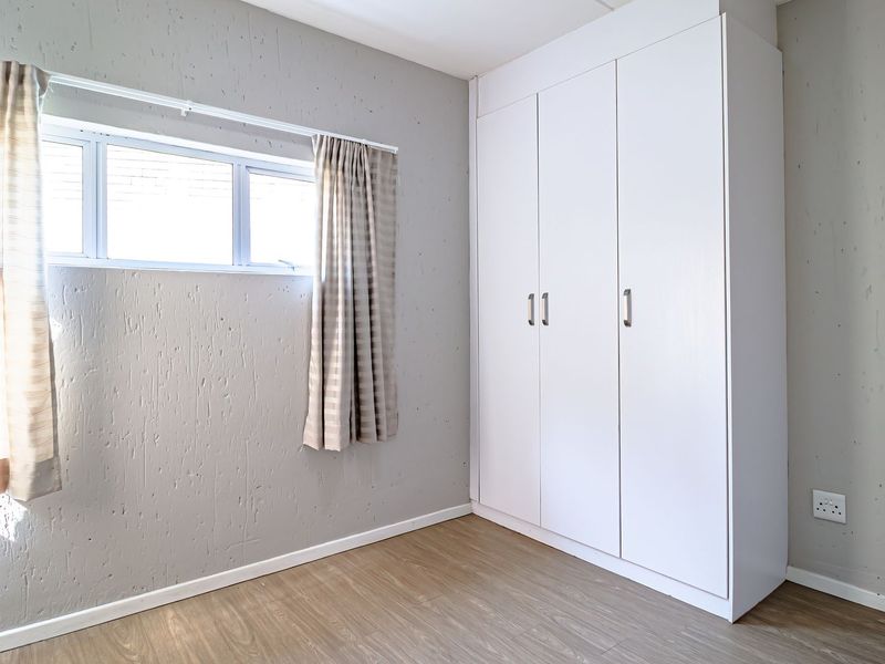 A clean, empty bedroom featuring light laminate flooring, textured grey walls, and a large white built-in wardrobe with ample storage space.