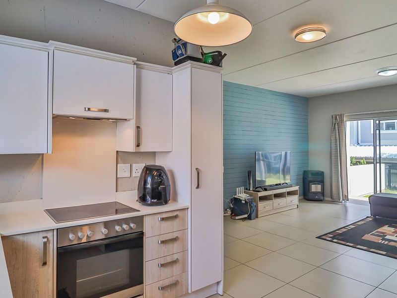 Open-plan living area featuring a modern kitchen with built-in appliances, tiled flooring, and direct access to an outdoor patio through sliding glass doors.