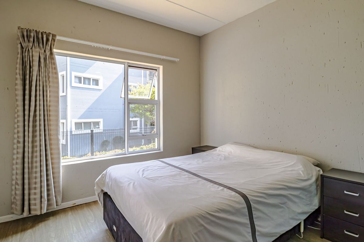 A bedroom featuring laminate flooring and a large window with natural light, providing a functional space for rest.