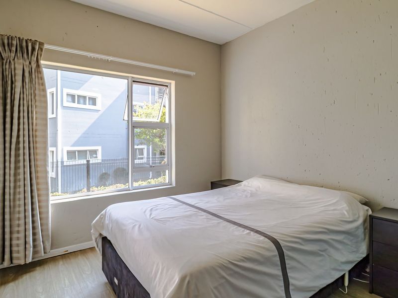 A bedroom featuring laminate flooring and a large window with natural light, providing a functional space for rest.