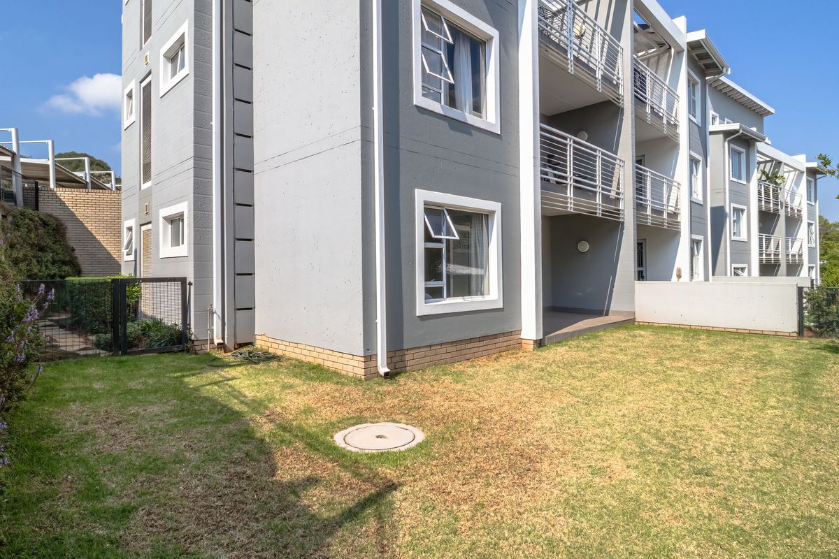 Rear view of a modern apartment complex featuring concrete facade, private balconies with metal railings, and a shared garden area.