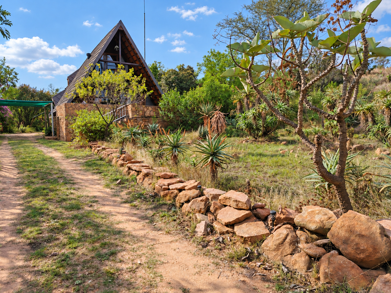 A charming A-frame townhouse featuring stone cladding and a natural garden setting with a stone retaining wall along the driveway.