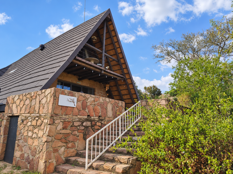 A charming A-frame townhouse featuring rustic stone cladding, a tiled roof, and an elevated balcony accessed by stone stairs with a white metal railing.