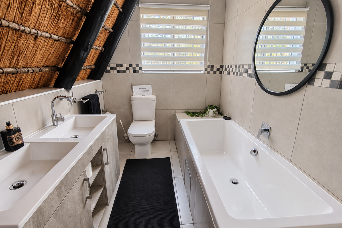 A modern bathroom featuring a double vanity, built-in bathtub, and toilet, highlighted by a unique thatched roof ceiling with exposed timber rafters.