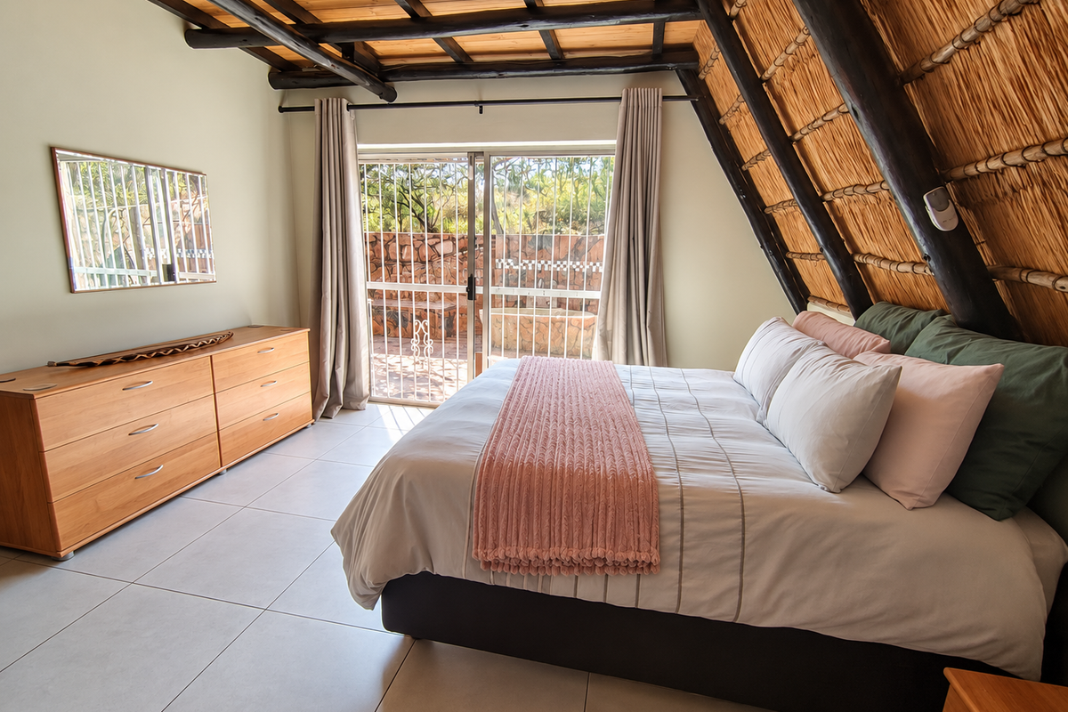 A well-maintained bedroom featuring exposed timber rafters, a unique thatched ceiling, tiled floors, and a sliding glass door providing access to the patio.