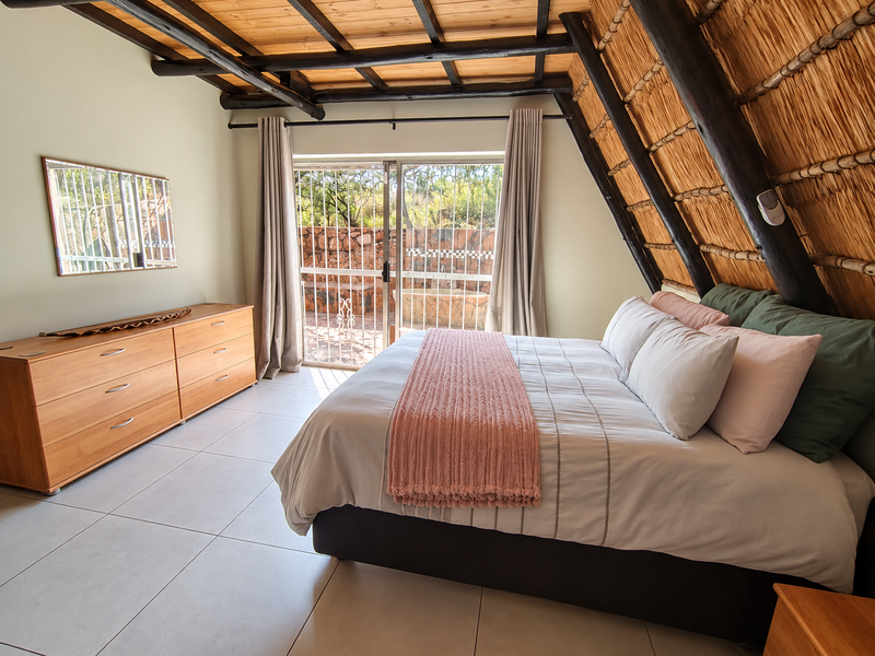 A well-maintained bedroom featuring exposed timber rafters, a unique thatched ceiling, tiled floors, and a sliding glass door providing access to the patio.