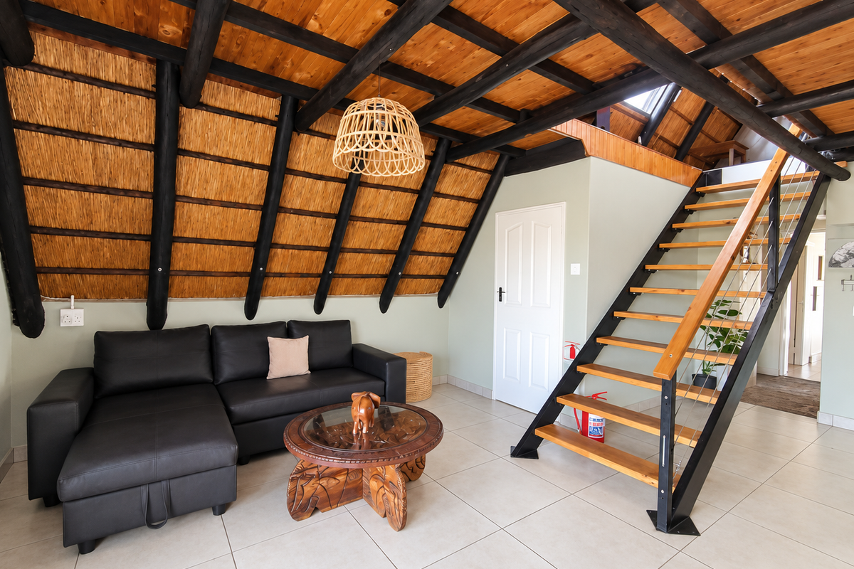 A bright living area featuring a unique thatched ceiling with exposed timber rafters, tiled flooring, and a modern staircase leading to the upper level.
