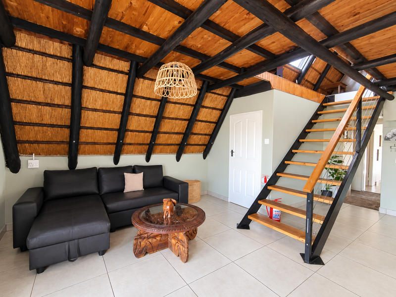 A bright living area featuring a unique thatched ceiling with exposed timber rafters, tiled flooring, and a modern staircase leading to the upper level.