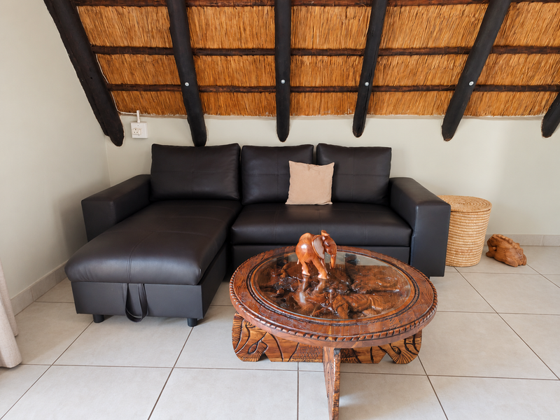 A cozy living area featuring a distinctive thatched roof with exposed timber rafters and neutral tiled flooring.
