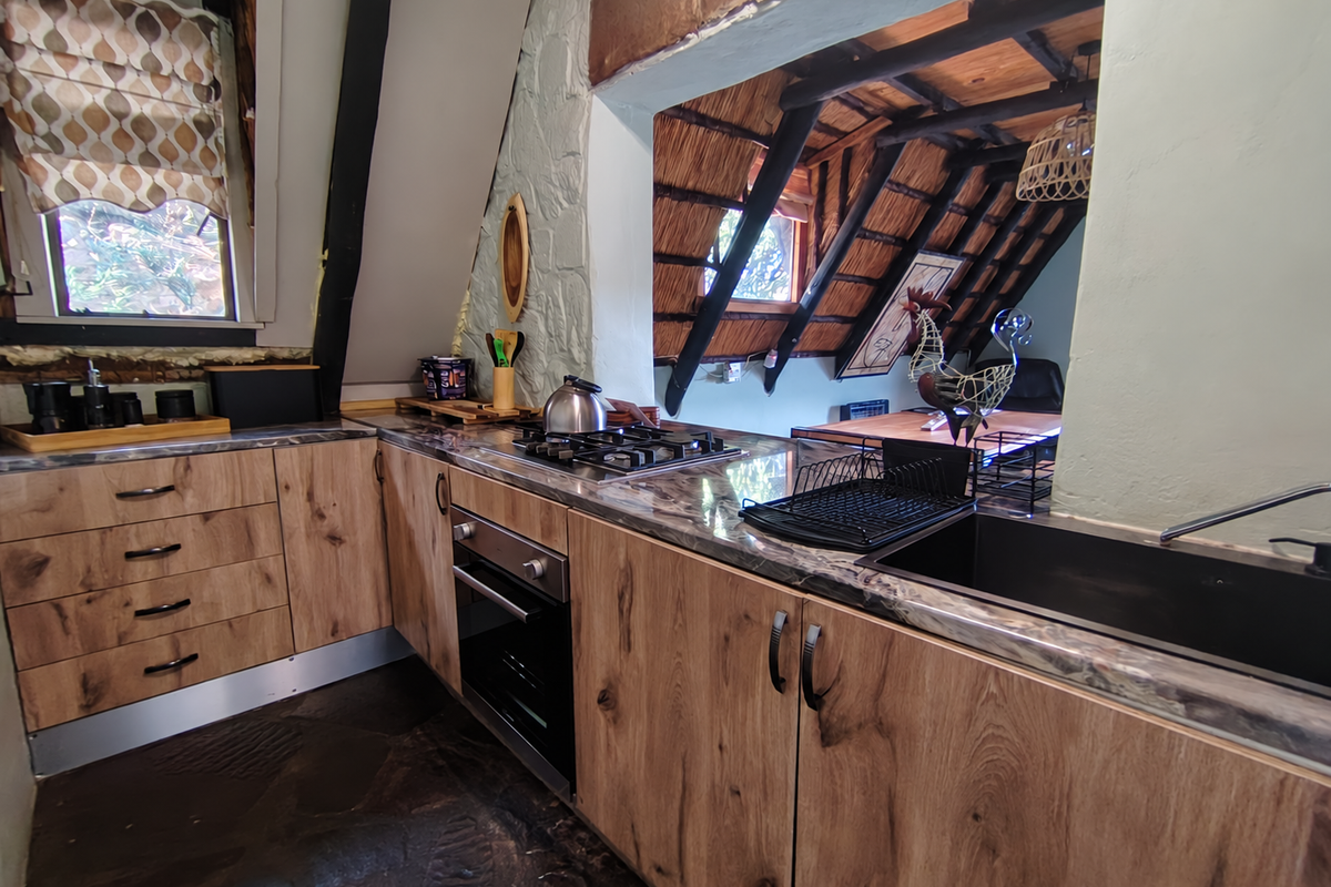 Rustic kitchen featuring wood-look cabinetry, stone-effect countertops, built-in oven, gas hob, and unique exposed timber rafters with a thatched ceiling design.