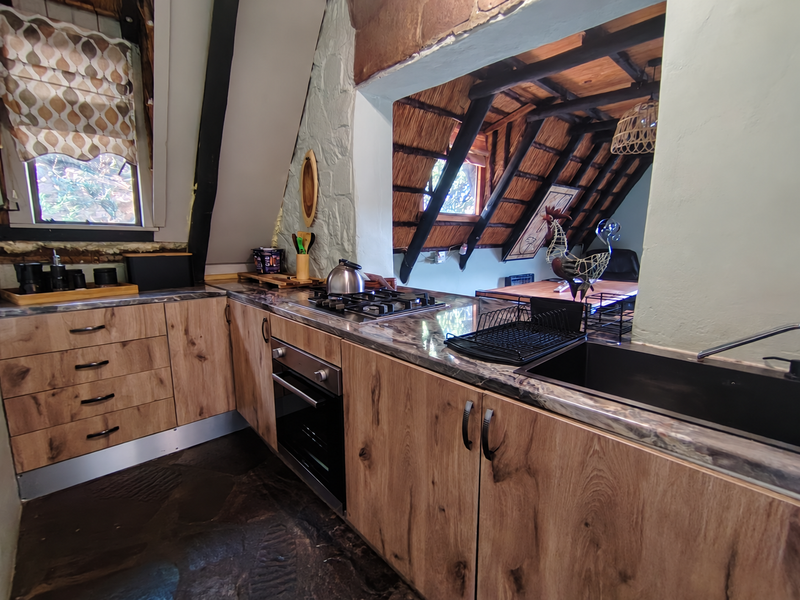 Rustic kitchen featuring wood-look cabinetry, stone-effect countertops, built-in oven, gas hob, and unique exposed timber rafters with a thatched ceiling design.