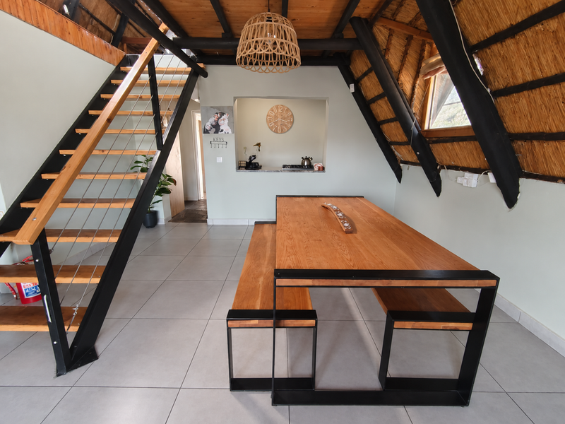 Open-plan living area featuring a striking A-frame design with exposed timber rafters, thatched ceiling, and a modern staircase leading to the upper level.