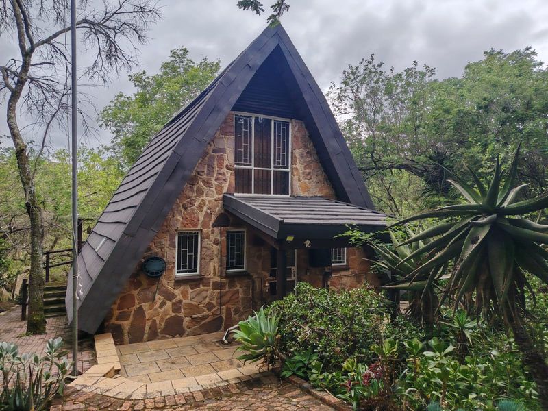 A charming A-frame townhouse featuring rustic stone cladding, a tiled roof, and a paved front patio surrounded by established garden greenery.