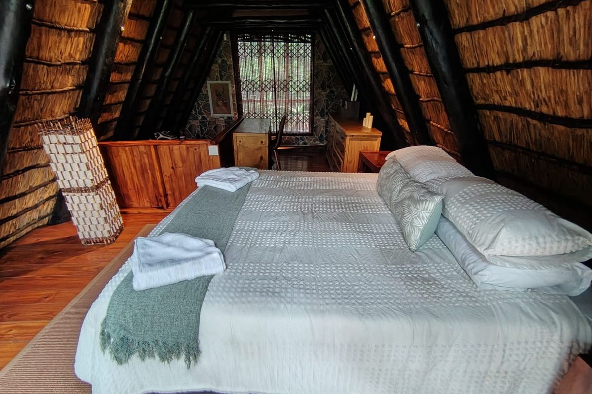 A cozy bedroom featuring a unique A-frame design with exposed timber rafters, a thatched roof interior, and warm timber flooring.