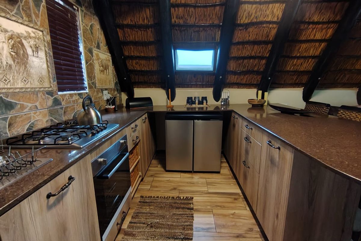 A unique kitchen featuring a rustic thatch roof, stone-tiled walls, timber cabinetry, and modern built-in appliances under a skylight.