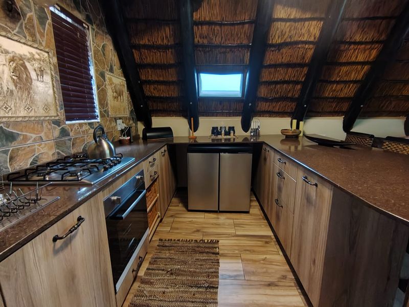 A unique kitchen featuring a rustic thatch roof, stone-tiled walls, timber cabinetry, and modern built-in appliances under a skylight.
