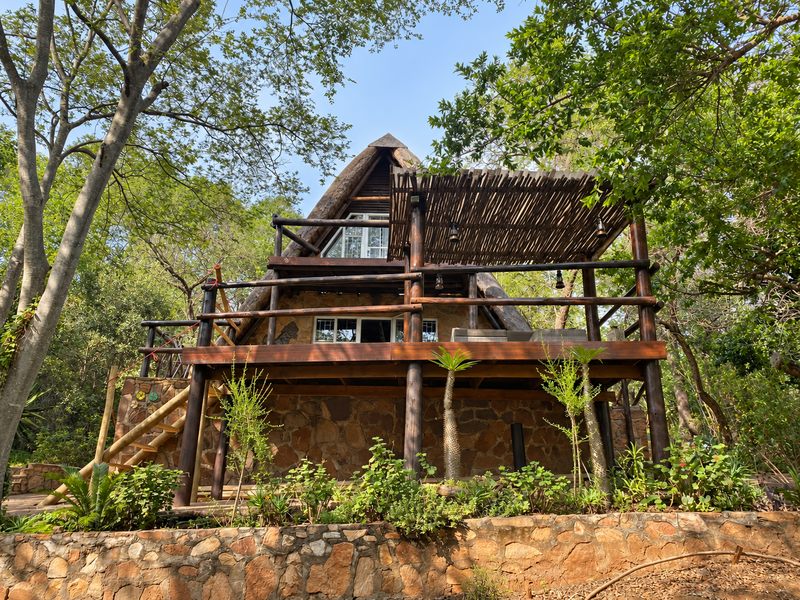 A rustic A-frame townhouse featuring stone cladding, a spacious timber deck with a pergola, and natural surroundings.