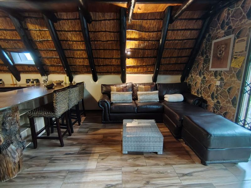 Open plan living area featuring a rustic thatched roof with exposed timber rafters, a stone feature wall, and a breakfast bar.