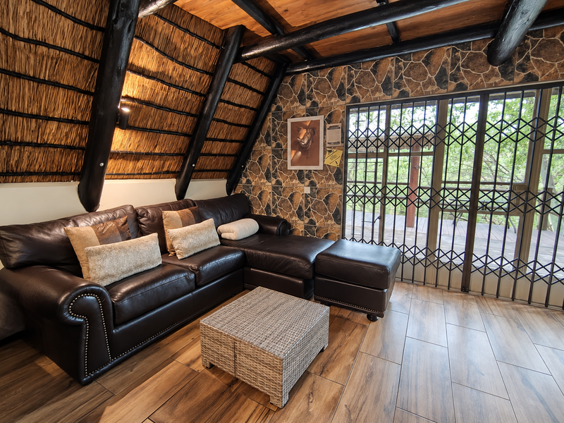 A cozy living room featuring a unique thatched ceiling with exposed timber beams, stone-clad feature wall, and direct access to an outdoor area via security gates.