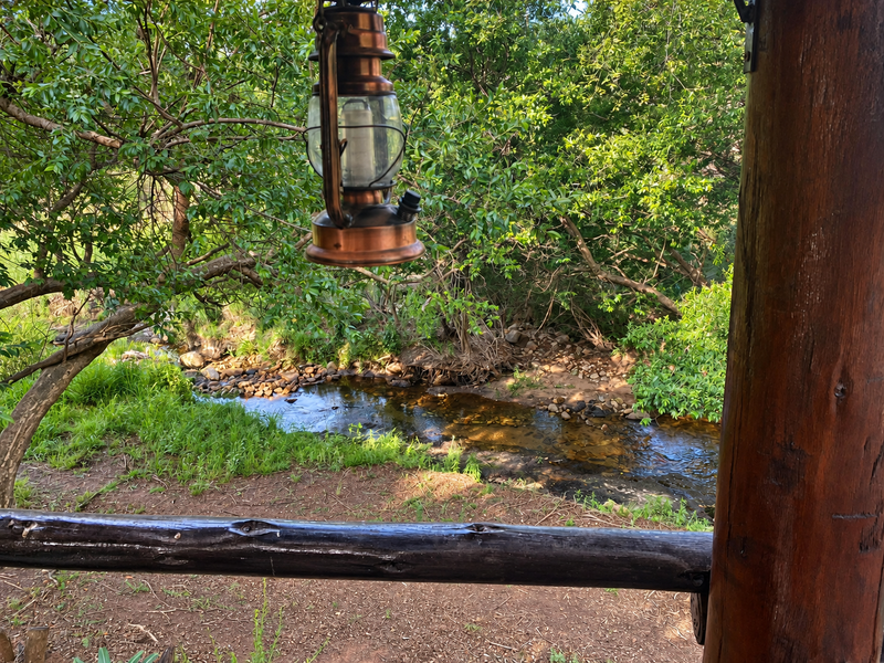 A scenic view of a natural stream and lush greenery, framed by a rustic timber railing and support post.