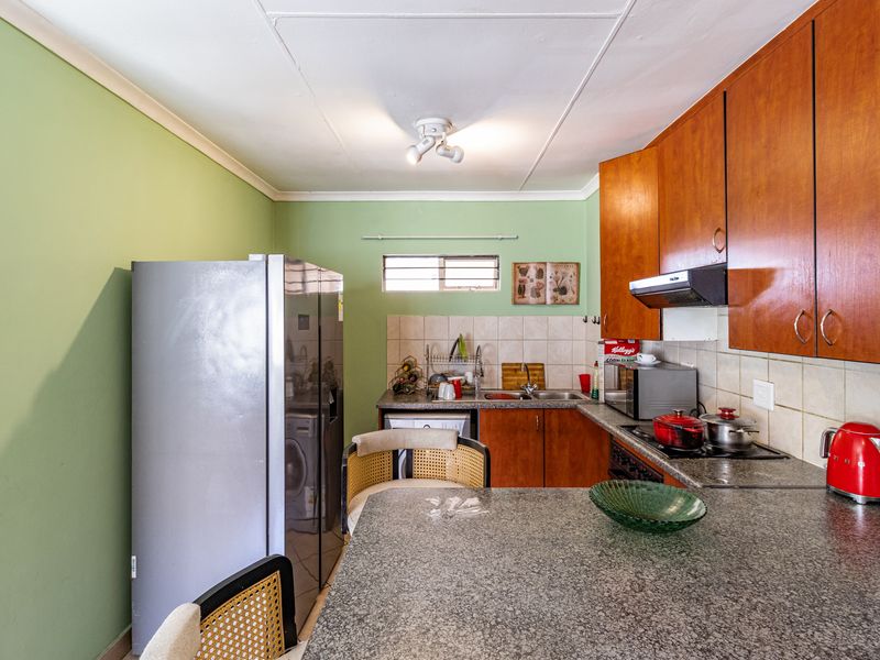 A functional kitchen featuring granite countertops, wooden cabinetry, a tiled backsplash, and an integrated extractor fan, offering a practical layout for daily use.