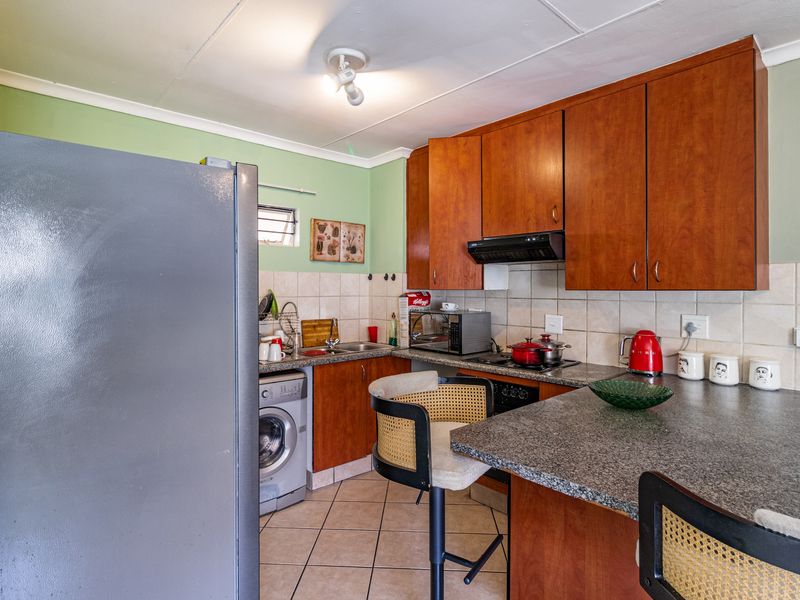 Compact kitchen featuring wooden cabinetry, granite countertops, tiled backsplash, and integrated appliances, offering a functional layout with tiled flooring.