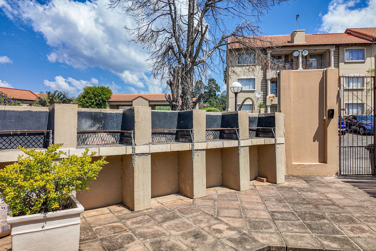 Communal outdoor area featuring a row of built-in brick braai stations on a paved patio within an apartment complex.