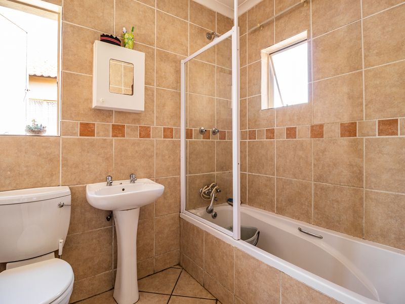 A functional bathroom featuring a pedestal basin, toilet, and a combined bathtub with a shower screen, finished with neutral wall and floor tiling.