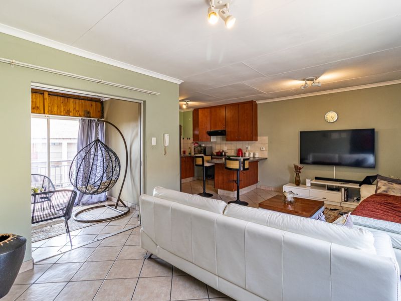 Open-plan living area featuring tiled floors, a functional kitchen with built-in cabinetry, and direct access to a balcony through sliding glass doors.