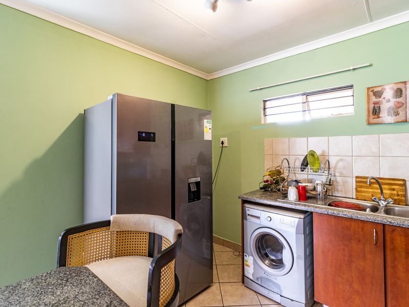 Compact kitchen area featuring built-in cabinetry, a stainless steel sink, tiled backsplash, and tiled flooring.