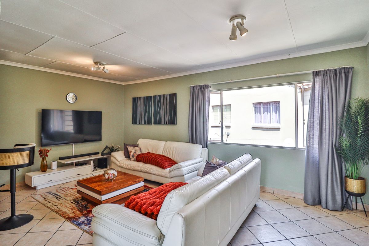 A comfortable living room featuring tiled flooring, large windows allowing natural light, and ceiling-mounted spotlights.