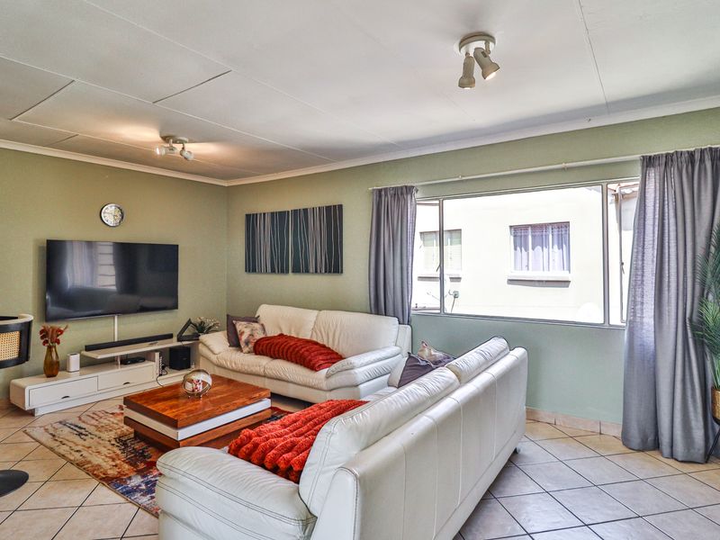 A comfortable living room featuring tiled flooring, large windows allowing natural light, and ceiling-mounted spotlights.