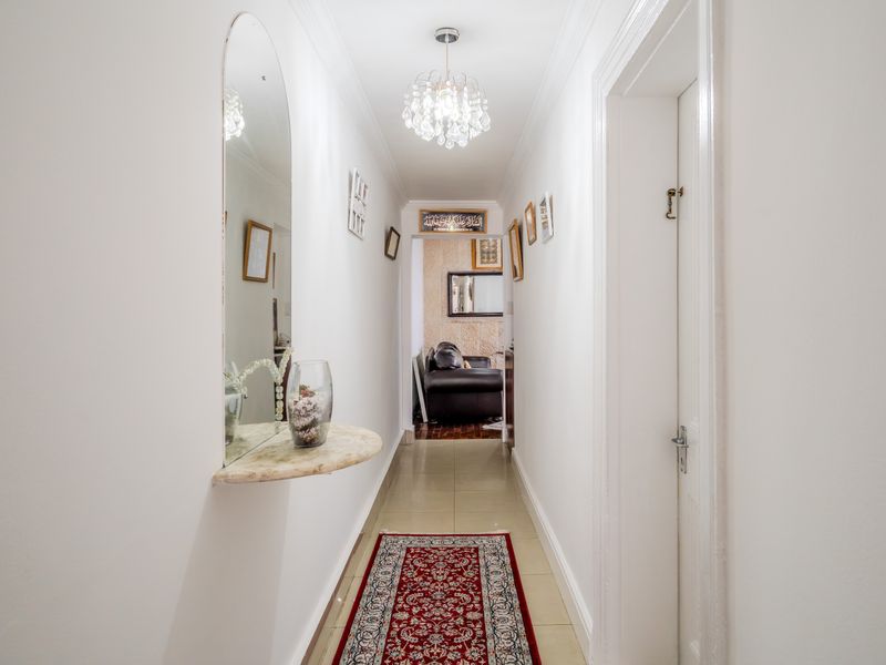 A well-maintained interior hallway featuring tiled flooring, decorative ceiling cornice, and a built-in wall mirror with a matching stone shelf.