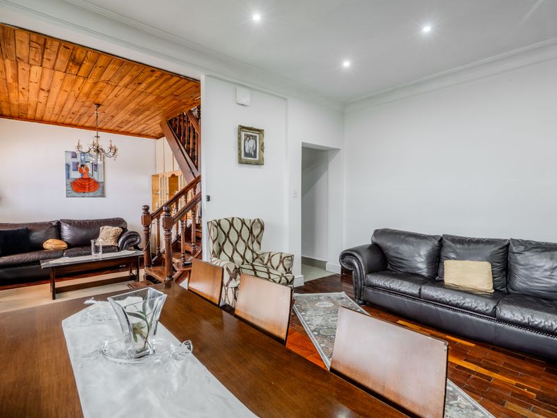 Spacious open-plan living and dining area featuring rich hardwood flooring, a distinctive timber-clad ceiling, and a classic wooden staircase.