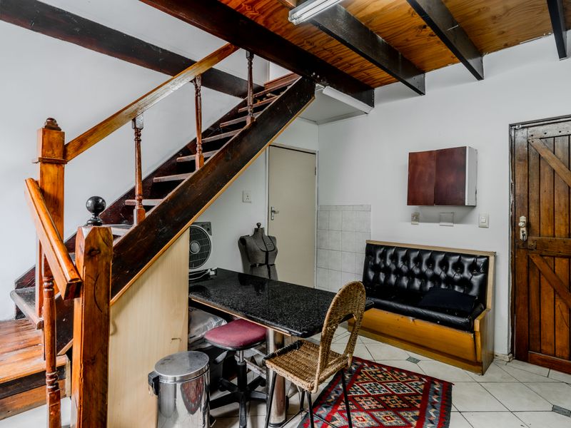 Living area featuring a wooden staircase, exposed ceiling beams, and tiled flooring, offering a rustic aesthetic with potential for modernization.
