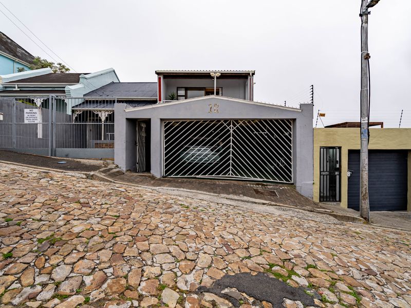 Front elevation of a townhouse featuring a secure garage, gated entrance, and electric fencing, situated on a sloped cobblestone street.