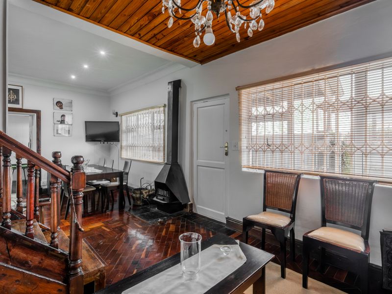 Open-plan living and dining area featuring warm parquet flooring, a timber-clad ceiling, a central fireplace, and a classic wooden staircase.