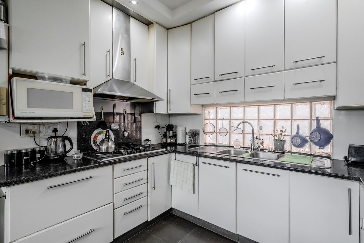 A functional kitchen featuring white cabinetry, granite countertops, a gas hob, stainless steel extractor fan, and a unique glass block window for natural light.